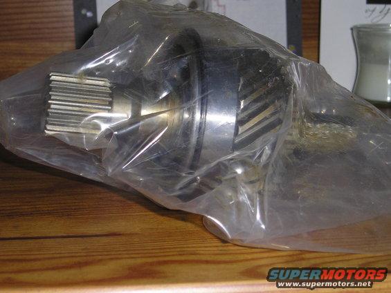 Metal gear with splines, wrapped in clear plastic, on a wooden surface