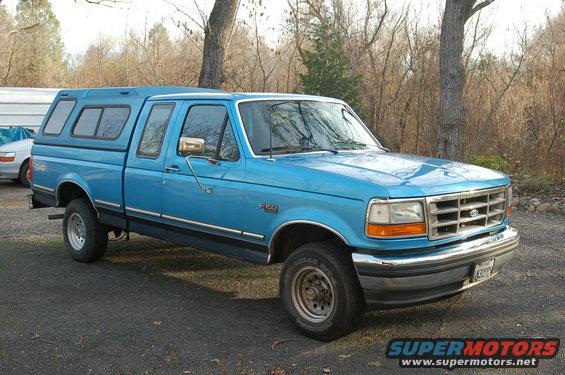 Blue 1992 Ford F-150 pickup truck with a camper shell, seen from the front-right angle