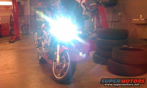 Red sport motorcycle with bright headlights on in a garage with stacked tires