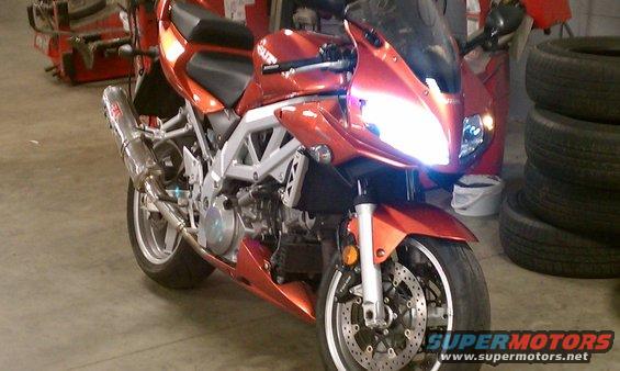 Orange 2003 Suzuki SV1000S motorcycle with aftermarket exhaust, parked indoors