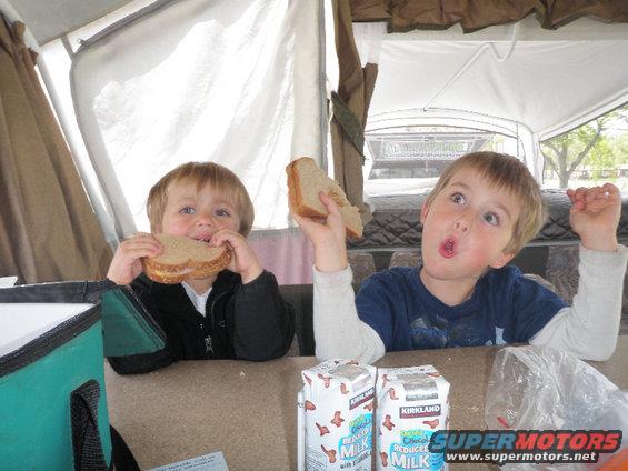 Two boys eating sandwiches inside a pop-up camper