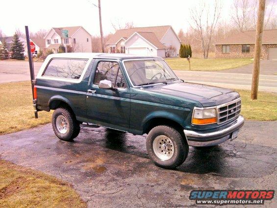 Green Ford Bronco parked on a wet driveway, white roof, chrome bumper