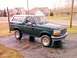 1993 Ford Bronco - This green Ford Bronco is parked on a wet driveway with houses in the background.