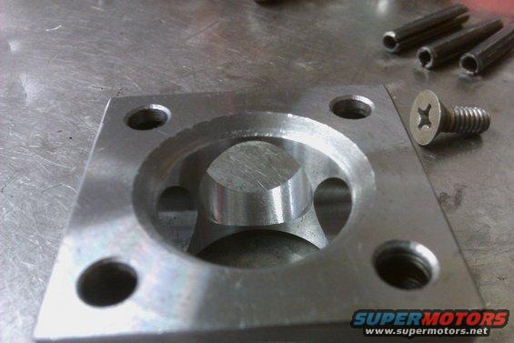 Close-up of a machined metal part with a screw and three pins nearby