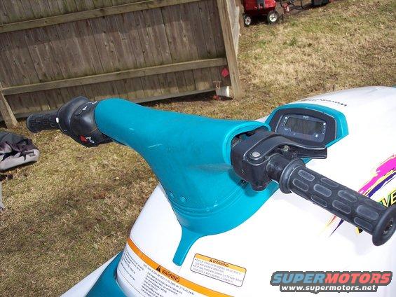 Jet ski handlebars with teal plastic cover and digital display. Warning labels visible