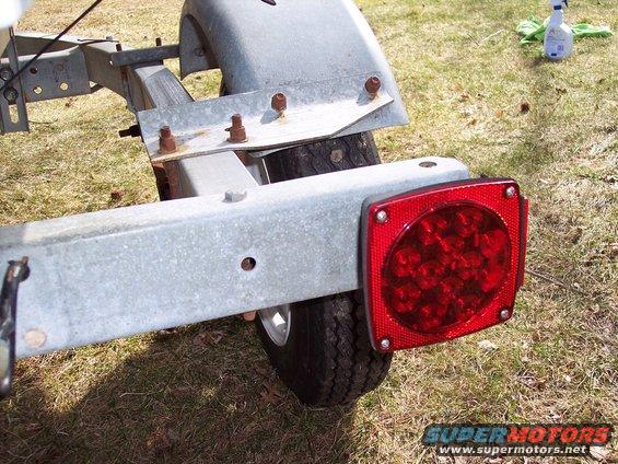 Boat trailer frame with a red LED tail light and tire visible. Supermotors.net logo in corner