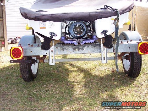 Jet ski on a trailer, rear view. The jet ski is covered with a black tarp. The trailer has two wheels and red taillights