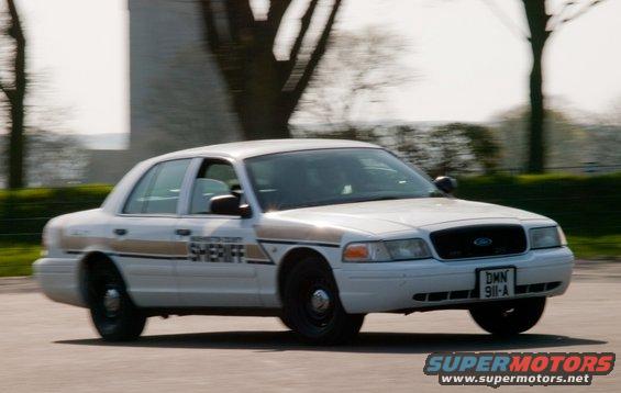 White 2001 Ford Crown Victoria sheriff's car in motion, front 3/4 view, showing 'WASHINGTON COUNTY SHERIFF' text and license plate 'DMN 911-A'