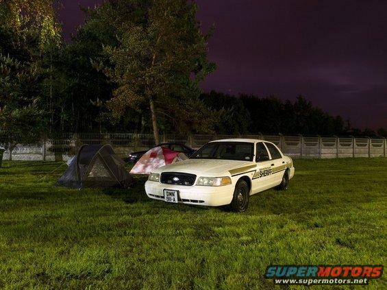 Ford Crown Victoria police car parked next to tents at night