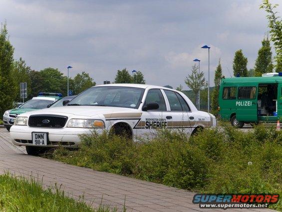White 2001 Ford Crown Victoria police car with 'Washington County Sheriff' text, parked next to a green police van