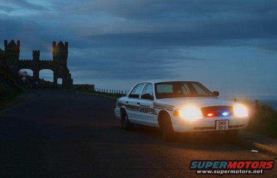 2001 Ford Crown Victoria police car with lights on, parked by a castle at dusk
