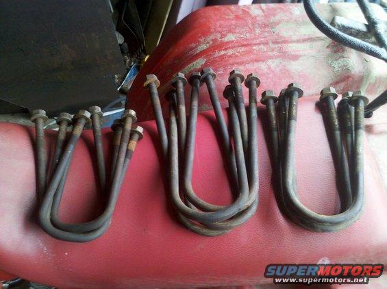 Several rusty U-bolts with nuts laid out on a red surface