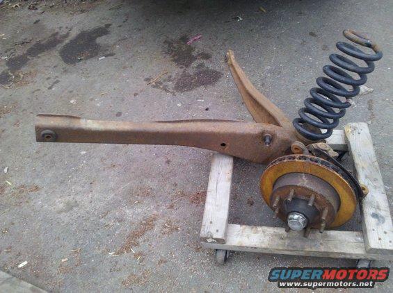 rusted suspension assembly with coil spring and brake rotor on a wooden dolly
