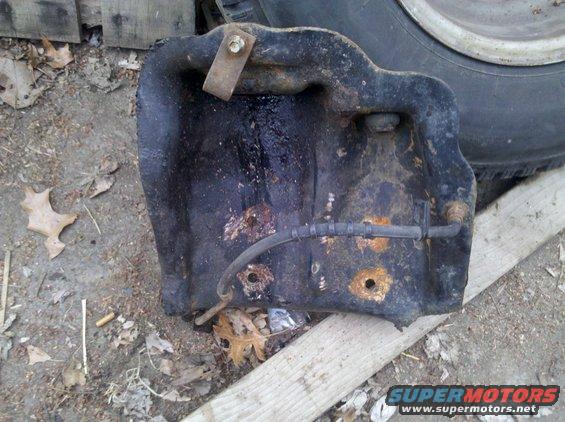 rusted metal part with a black hose attached, lying on the ground near leaves and wood