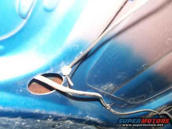 Close-up of blue painted metal under a hood with wiring and a grommet