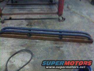 Rock sliders mounted on a wooden plank, with a Supermotors.net logo at the bottom right