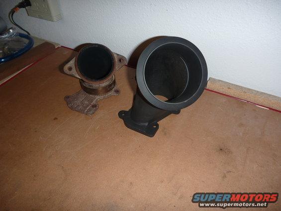 Two exhaust pipe components, one rusted metal and one black, on a wooden surface