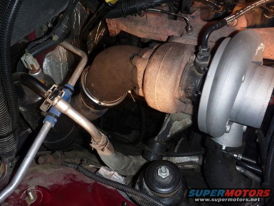 Close-up of a turbocharger and associated engine plumbing. Some parts look rusty, others are shiny