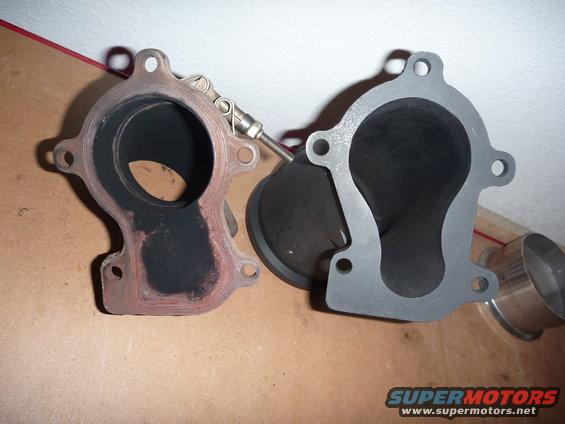 Two exhaust manifold flanges, one with carbon buildup and a sensor, on a wooden surface