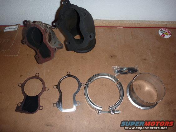 Turbocharger exhaust housing, gaskets, V-band clamp, and adapter pipe on a wooden surface