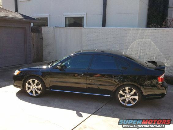 Black sedan parked in a driveway, side view. Sun glare on the paint