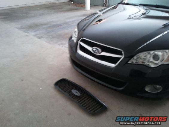 Black Subaru Legacy with its front grille removed and placed on the ground
