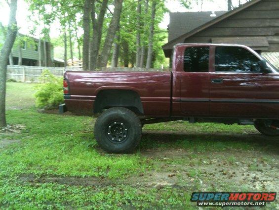 Side view of a maroon pickup truck with large off-road tires and tinted windows