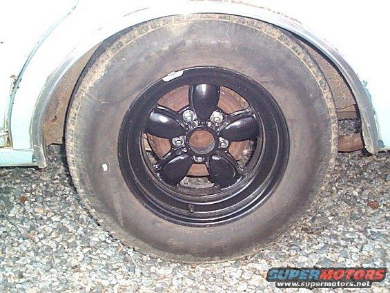 Close-up of a black five-spoke wheel and worn tire on gravel