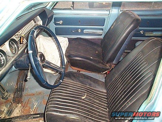 1966 Oldsmobile Cutlass interior with blue dashboard, black ribbed seats, and rust on the floor