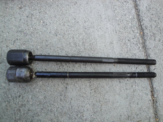 Two tie rod ends, one with a hexagonal joint and the other with a rounded joint, laid on concrete