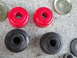 2003 Ford Taurus - Comparison of new red polyurethane and old black rubber suspension bushings laid out on a concrete surface.
