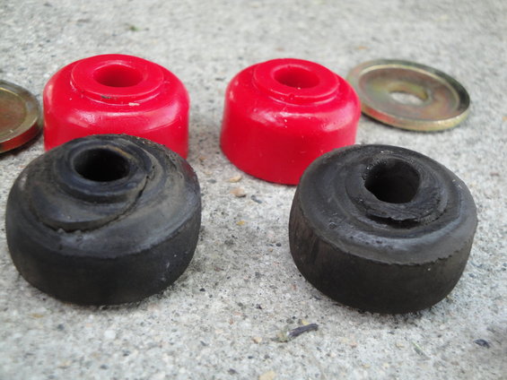 Two old black rubber bushings and two new red polyurethane bushings with a metal washer