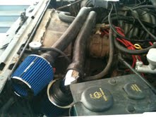 Engine bay with blue cone air filter, black hoses, and various engine components. The condition appears used