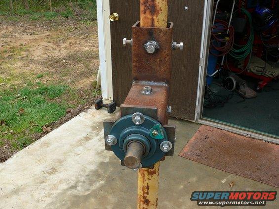 Rusted metal assembly with a blue bearing and shaft, attached to a yellow pole