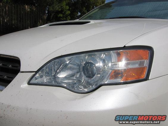 Front of a white Subaru Legacy with a hood scoop and clear headlights