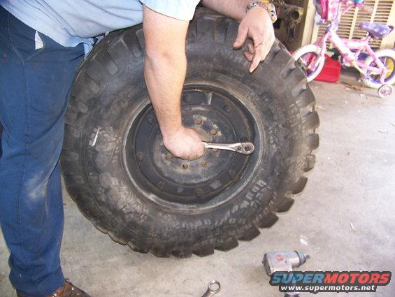 Large tire with a socket wrench being used on its lug nuts. A pink bicycle is in the background