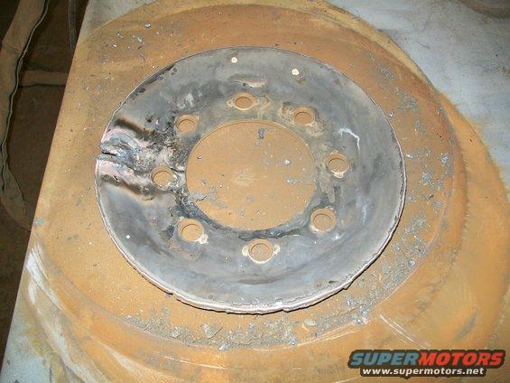 Damaged metal wheel hub with rust and weld marks, showing bolt holes