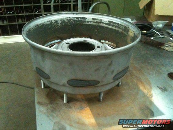 Custom metal wheel rim with multiple lug holes and welded accents, resting on metal legs