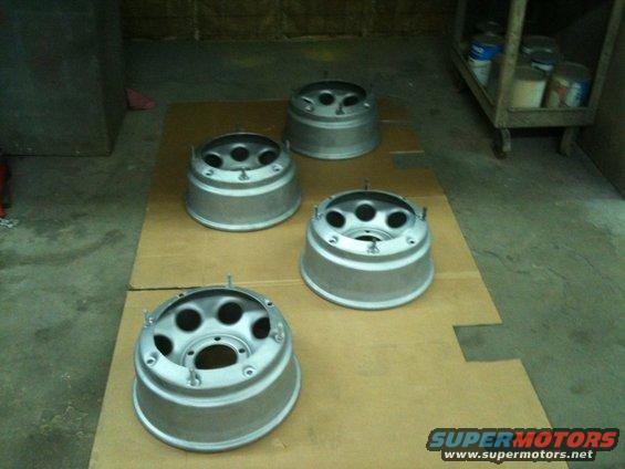 Four silver metal wheel rims with five lug holes each, laid out on cardboard