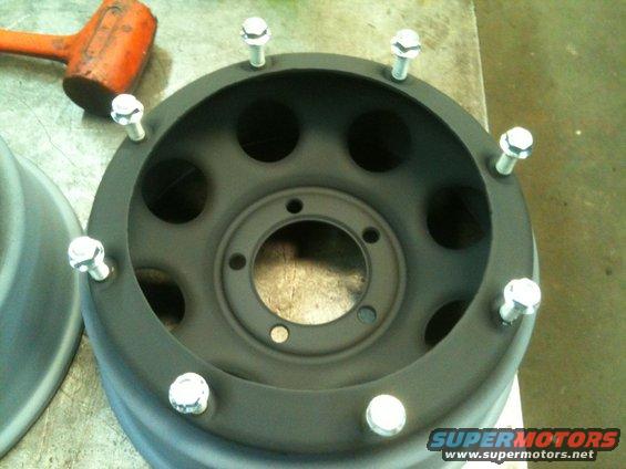 Black steel wheel with lug nuts and a rubber mallet nearby