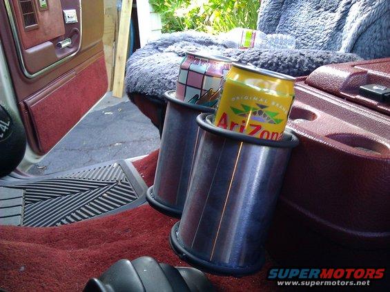 Interior shot of a vehicle showing two cans in cup holders, one Arizona Iced Tea. Door panel and seat visible