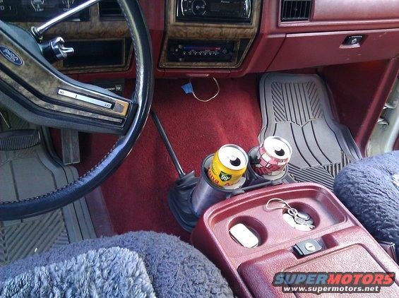 Vehicle interior with red carpet, gray floor mats, and a maroon center console holding keys and two soda cans