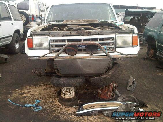 White Ford Bronco with hood open, aftermarket bumper, and missing tires