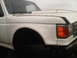 1986 Ford Bronco - Front corner view of a white truck, showing the fender, headlight, and part of the grille. The vehicle appears to be from around 1987.