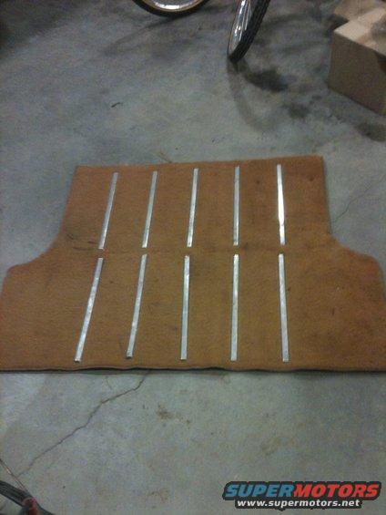 Brown carpet mat with silver strips, lying on concrete floor