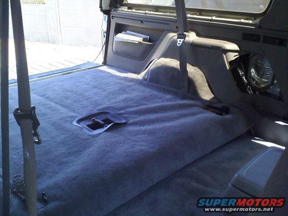 Vehicle interior with gray carpet, seat belts, and a storage compartment