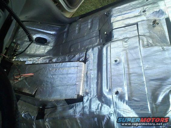 Car floor covered in silver sound deadening material, wires visible