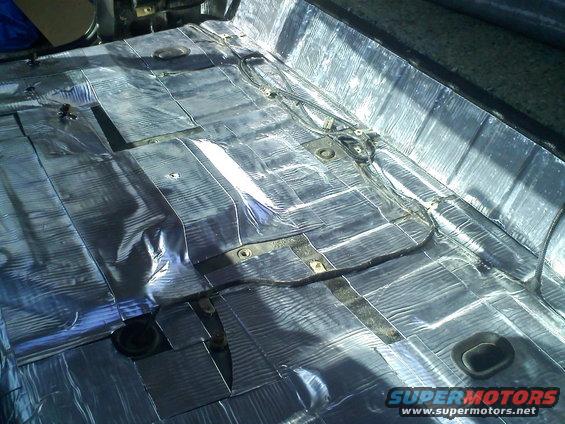 Vehicle interior floor covered in silver insulation material with visible wiring and black grommets