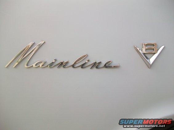 Chrome "Mainline" script emblem and V8 badge on a light-colored car
