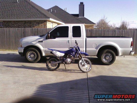 2003 Ford F-250 pickup truck parked next to a blue dirt bike on a concrete driveway